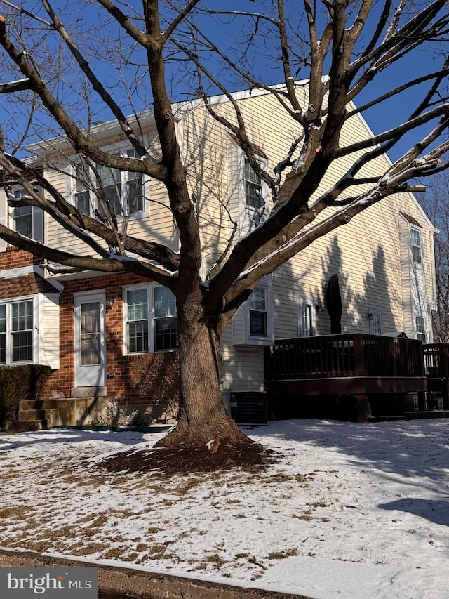 view of snow covered exterior with brick siding and central AC unit