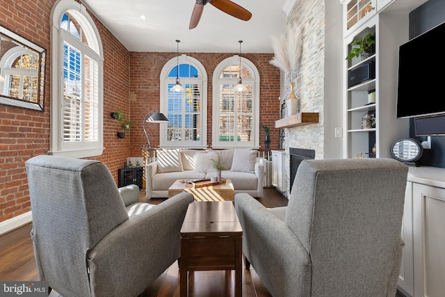 living room with brick wall, a fireplace, a ceiling fan, and dark wood-type flooring