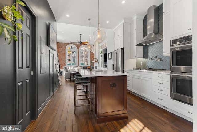 kitchen with dark wood-style floors, light countertops, appliances with stainless steel finishes, a sink, and wall chimney exhaust hood