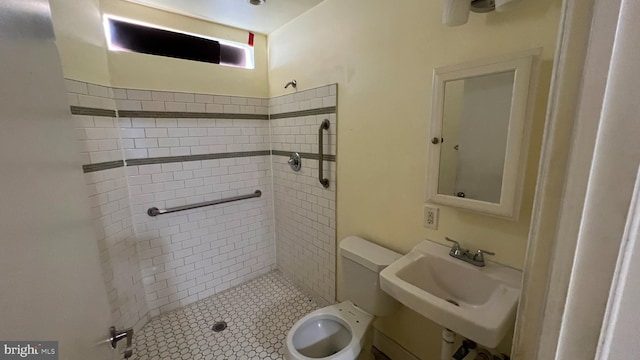 bathroom with sink, a tile shower, and toilet