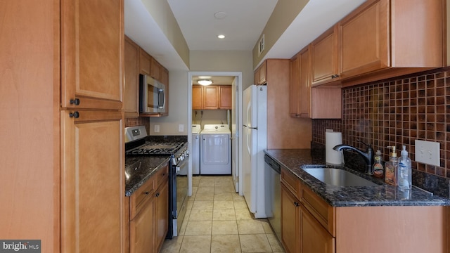 kitchen featuring dark stone countertops, stainless steel appliances, washing machine and clothes dryer, and sink