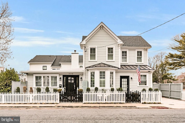 view of front of house featuring metal roof, a fenced front yard, roof with shingles, a standing seam roof, and a chimney