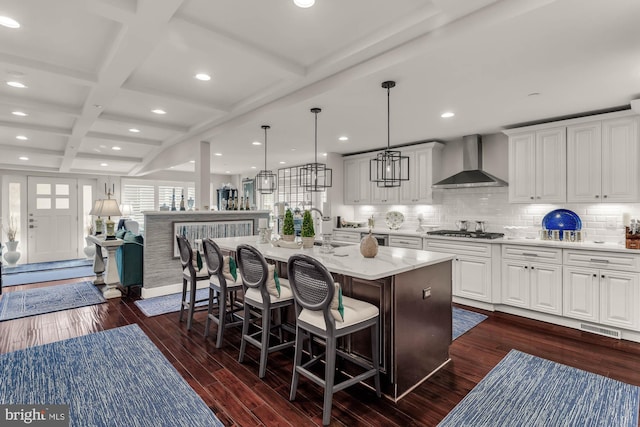 kitchen featuring wall chimney exhaust hood, a breakfast bar, dark wood-type flooring, beamed ceiling, and stainless steel gas cooktop