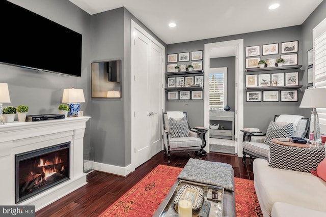 living area featuring a warm lit fireplace, dark wood-style flooring, recessed lighting, and baseboards