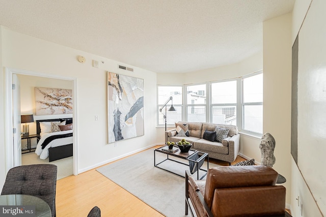 living room featuring baseboards, light wood-style flooring, visible vents, and a textured ceiling