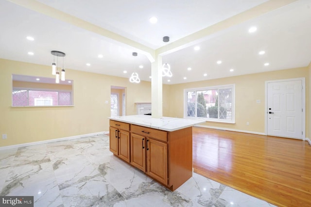 kitchen featuring a center island, marble finish floor, brown cabinets, hanging light fixtures, and light stone countertops