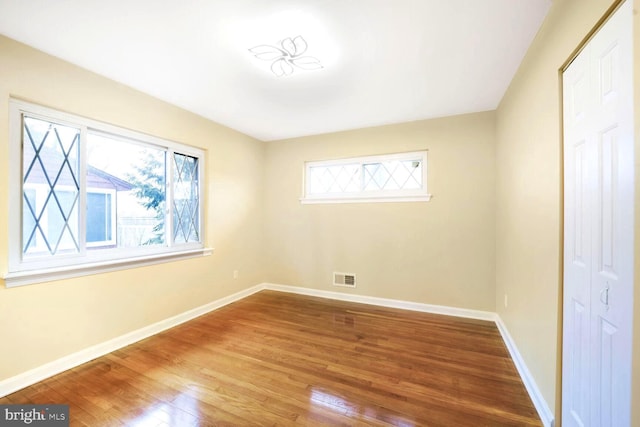 empty room featuring wood finished floors, visible vents, and baseboards