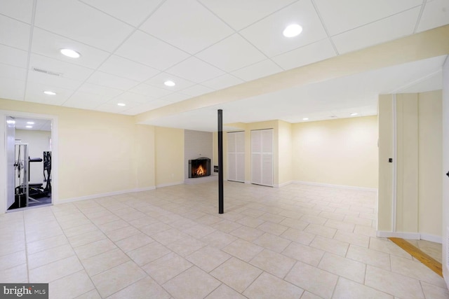 finished below grade area featuring a paneled ceiling, a brick fireplace, baseboards, and recessed lighting