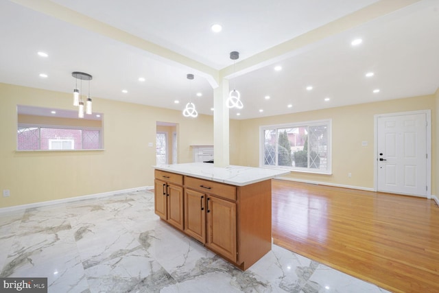 kitchen featuring light stone counters, marble finish floor, a center island, brown cabinetry, and decorative light fixtures