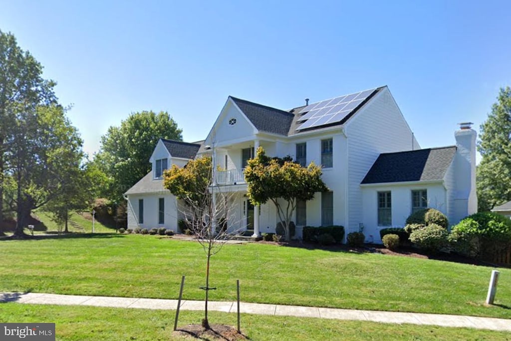 view of front of home featuring solar panels, a front yard, and a balcony