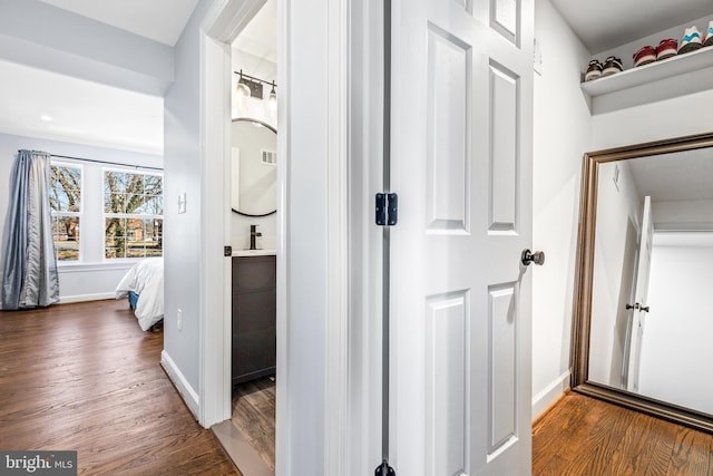 corridor with dark wood-style flooring, visible vents, and baseboards