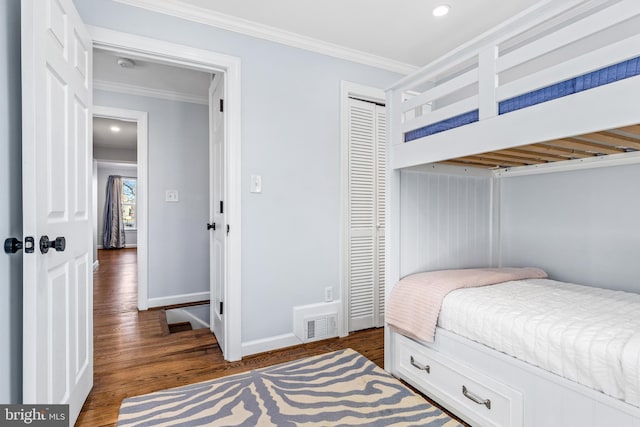 bedroom with dark wood-style floors, crown molding, a closet, visible vents, and baseboards