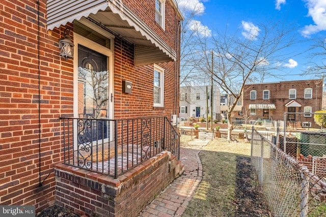 entrance to property featuring brick siding, fence, and a residential view