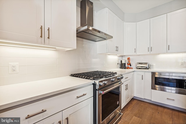 kitchen with appliances with stainless steel finishes, dark wood-type flooring, white cabinets, wall chimney range hood, and decorative backsplash