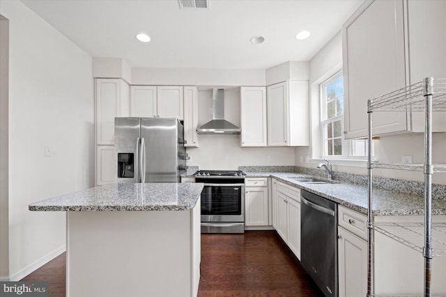 kitchen with sink, white cabinets, light stone counters, appliances with stainless steel finishes, and wall chimney range hood