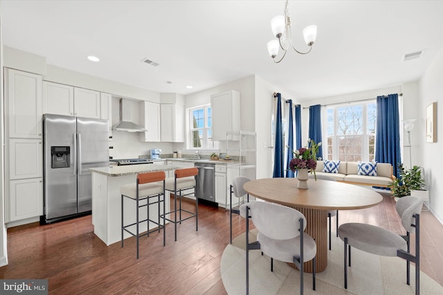 kitchen featuring dark wood-type flooring, stainless steel appliances, white cabinetry, and wall chimney range hood