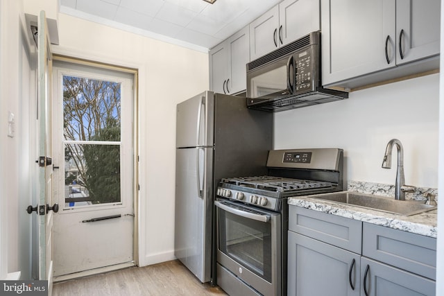 kitchen featuring light wood finished floors, stainless steel range with gas stovetop, gray cabinetry, black microwave, and a sink