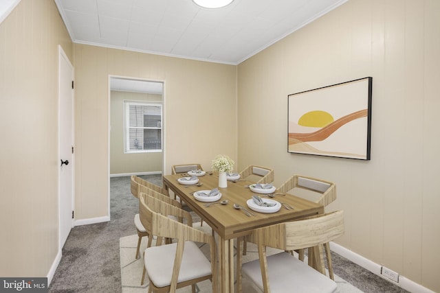 carpeted dining room with ornamental molding and baseboards