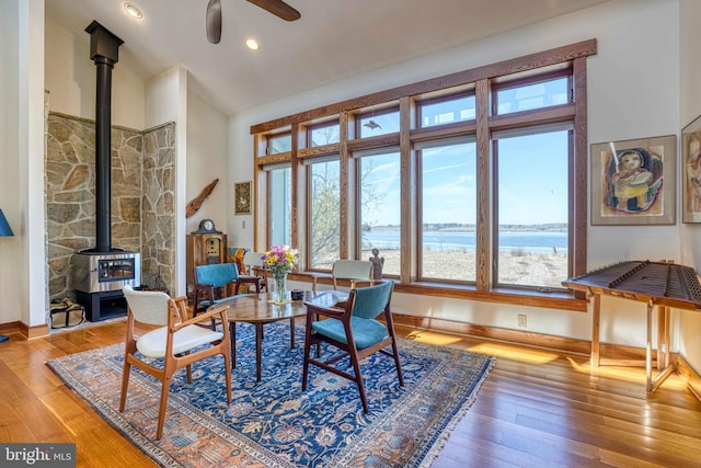 living room featuring baseboards, ceiling fan, a wood stove, wood finished floors, and high vaulted ceiling