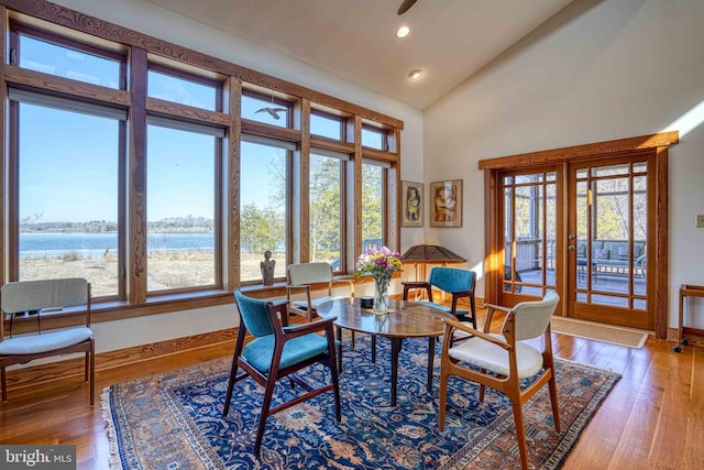 dining room featuring baseboards, a water view, light wood-type flooring, recessed lighting, and high vaulted ceiling