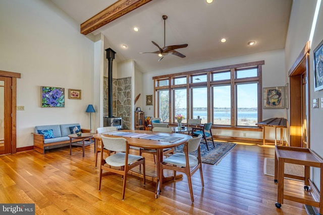 dining space with a ceiling fan, high vaulted ceiling, light wood-style flooring, and a wood stove