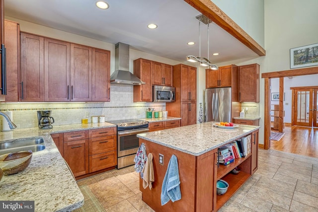 kitchen with a center island, light stone countertops, stainless steel appliances, wall chimney exhaust hood, and a sink