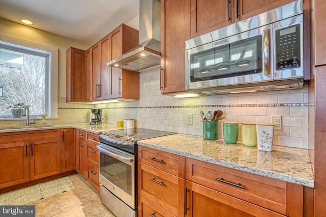 kitchen with tasteful backsplash, wall chimney range hood, brown cabinetry, stainless steel appliances, and a sink