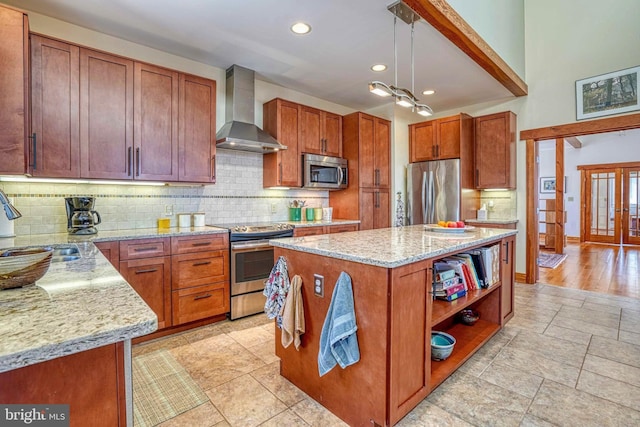 kitchen with backsplash, a center island, wall chimney range hood, light stone countertops, and stainless steel appliances