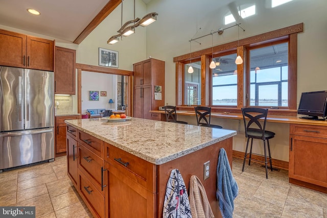 kitchen with light stone countertops, brown cabinetry, a kitchen island, freestanding refrigerator, and backsplash