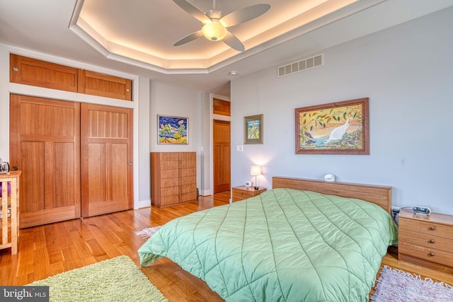 bedroom featuring visible vents, light wood-type flooring, a tray ceiling, a closet, and ceiling fan