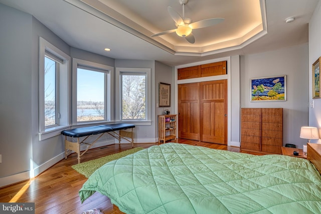 bedroom featuring a closet, a raised ceiling, baseboards, and wood finished floors