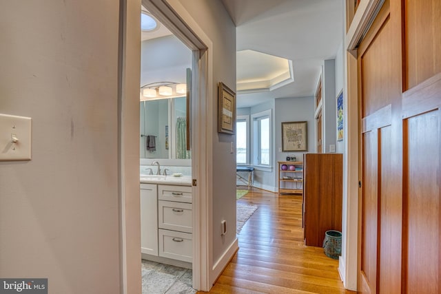 hall featuring light wood-style flooring, baseboards, and a sink