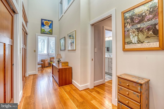 corridor with a towering ceiling, baseboards, light wood finished floors, and a sink