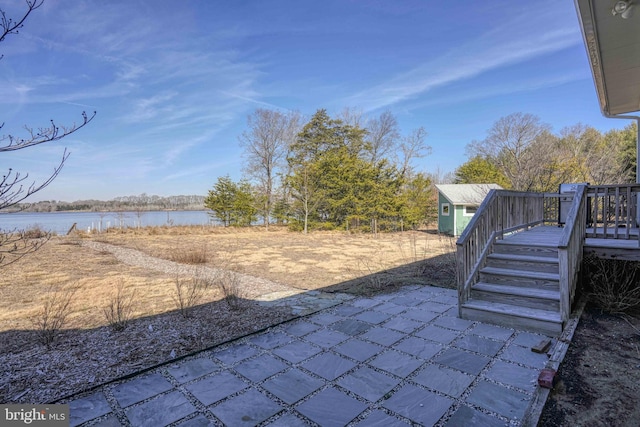 view of patio with an outbuilding, a storage shed, and a deck with water view