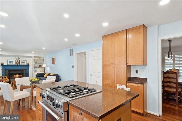 kitchen featuring wood finished floors, visible vents, stainless steel range with gas cooktop, a warm lit fireplace, and open floor plan