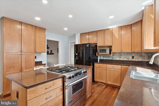 kitchen featuring backsplash, dark stone counters, wood finished floors, high end stainless steel range, and a sink