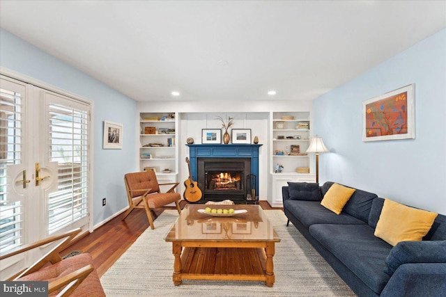 living area featuring built in features, wood finished floors, baseboards, recessed lighting, and a lit fireplace