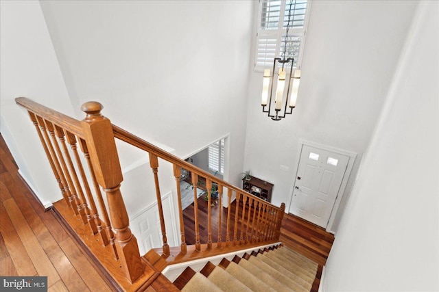 staircase with a high ceiling, a notable chandelier, and wood finished floors