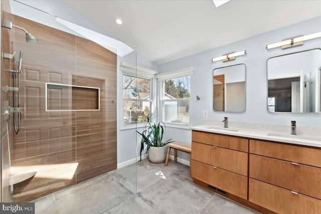 bathroom featuring double vanity, a walk in shower, baseboards, and a sink