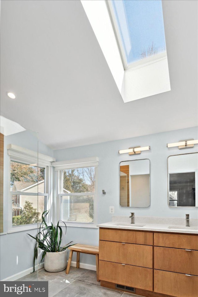 full bath with double vanity, a skylight, baseboards, and a sink