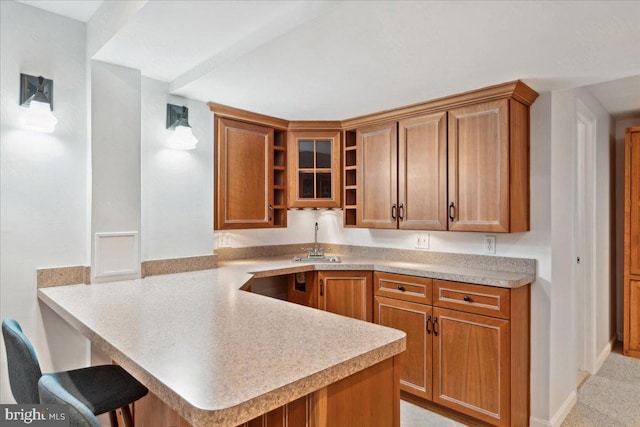 kitchen featuring open shelves, a breakfast bar area, a peninsula, brown cabinetry, and a sink