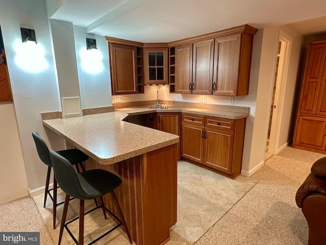 kitchen featuring a kitchen bar, brown cabinets, a peninsula, light countertops, and baseboards