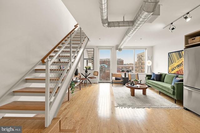 living area with stairs, light wood finished floors, track lighting, and a city view