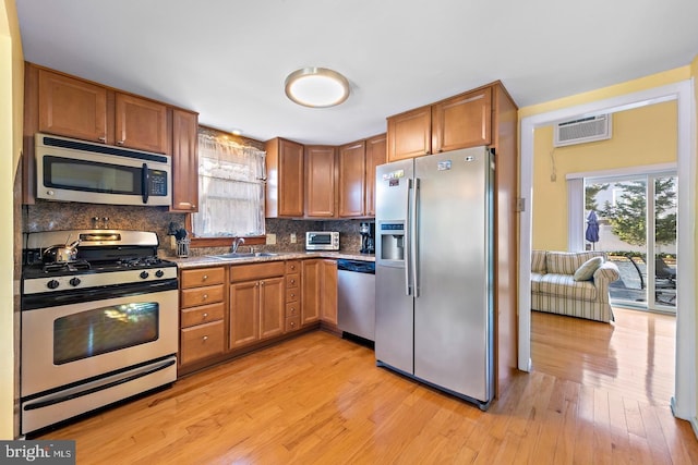 kitchen with appliances with stainless steel finishes, tasteful backsplash, light wood-type flooring, an AC wall unit, and sink