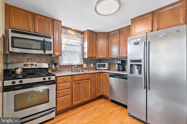 kitchen with light stone countertops, light hardwood / wood-style floors, sink, tasteful backsplash, and appliances with stainless steel finishes