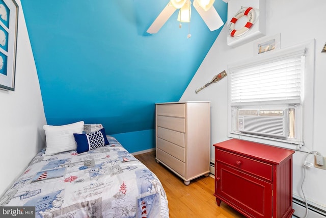 bedroom featuring light hardwood / wood-style floors, vaulted ceiling, cooling unit, and a baseboard radiator