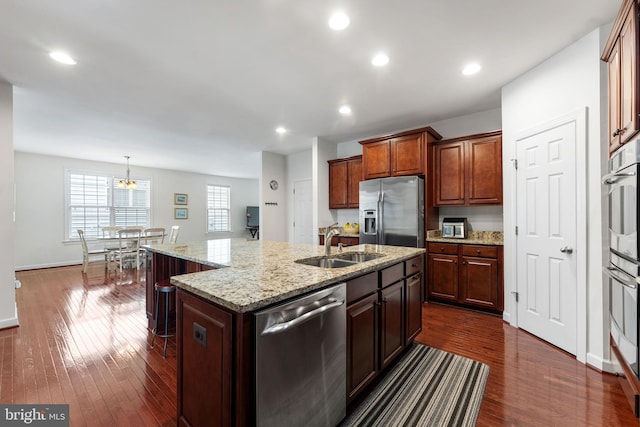 kitchen featuring appliances with stainless steel finishes, sink, decorative light fixtures, dark wood-type flooring, and a kitchen island with sink