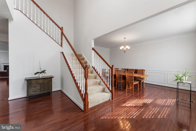 stairway featuring ornamental molding, hardwood / wood-style floors, a towering ceiling, and an inviting chandelier