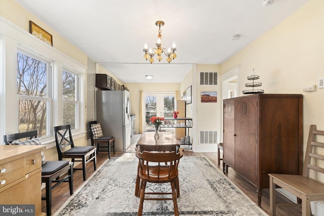 dining room with french doors, visible vents, an inviting chandelier, and wood finished floors