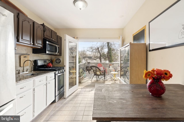 kitchen with tasteful backsplash, white cabinets, stainless steel appliances, a sink, and light tile patterned flooring